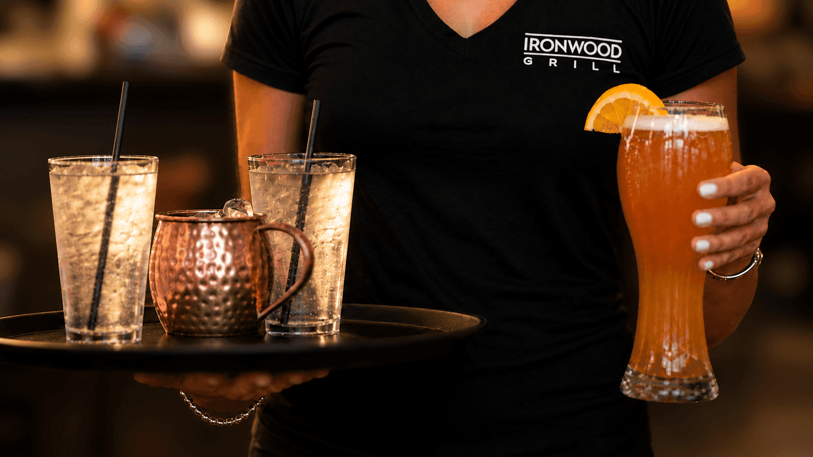A waitress carrying a beer and tray of drinks to a table